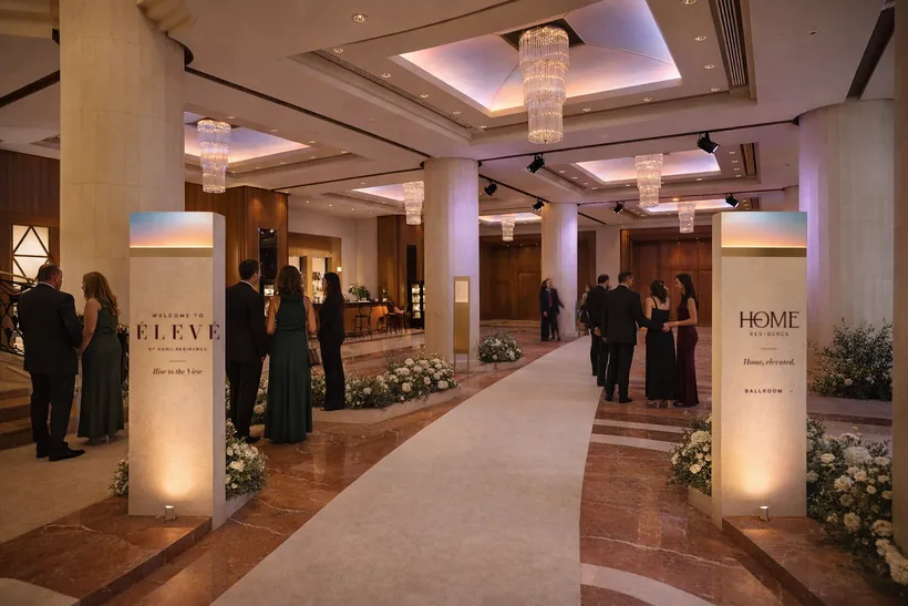 Entrance welcome signage — Twin limestone monoliths with a sky-glow crown frame the cream entrance runner: “Welcome to ÉLEVÉ” on one, Home Residence on the other